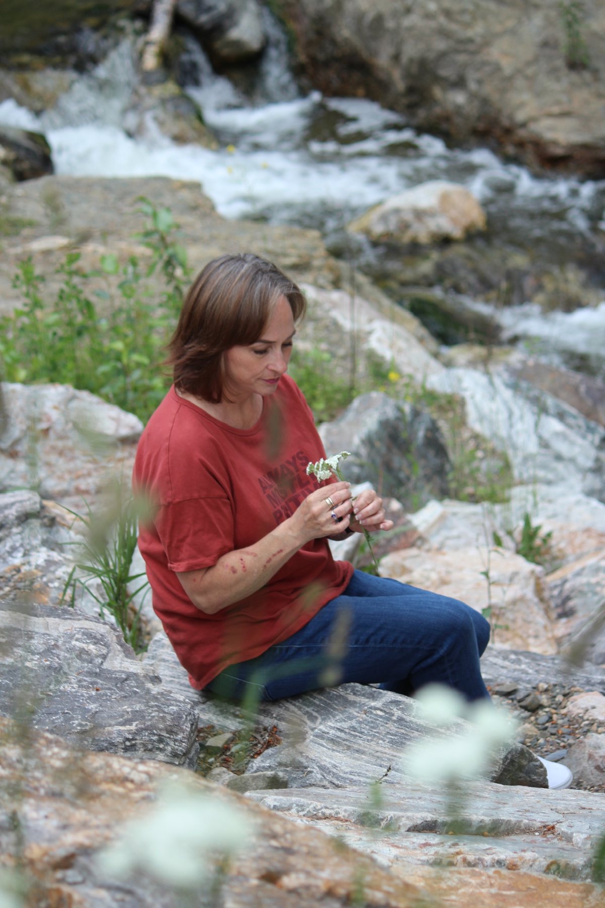 Jeunesse Pearson sitting by a creek holding wildflowers